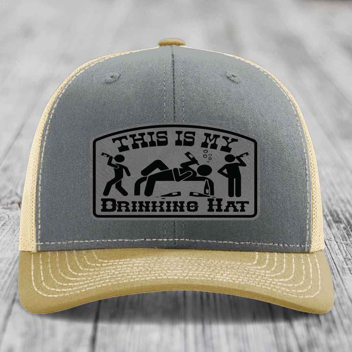 Grey and beige trucker hat with black leatherette patch reading &
