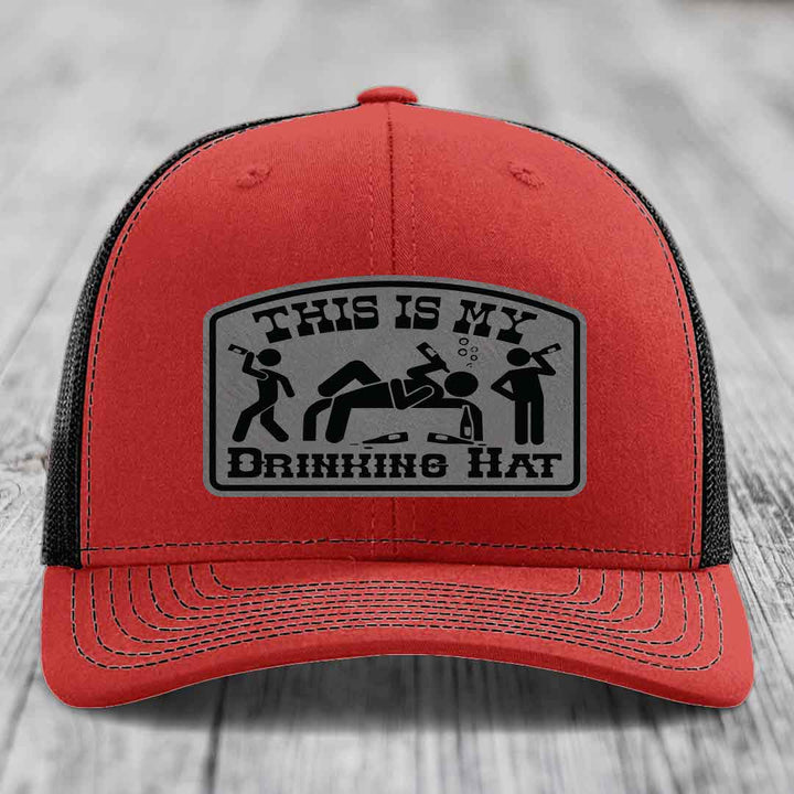Red trucker hat with black mesh back and a grey leatherette patch reading &