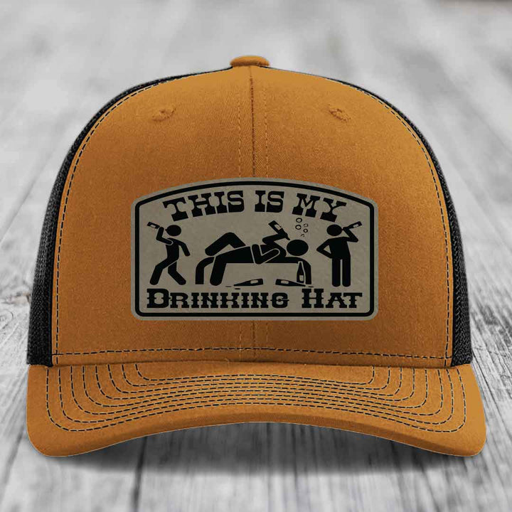 Tan trucker hat with black mesh back and a rectangular leatherette patch reading &