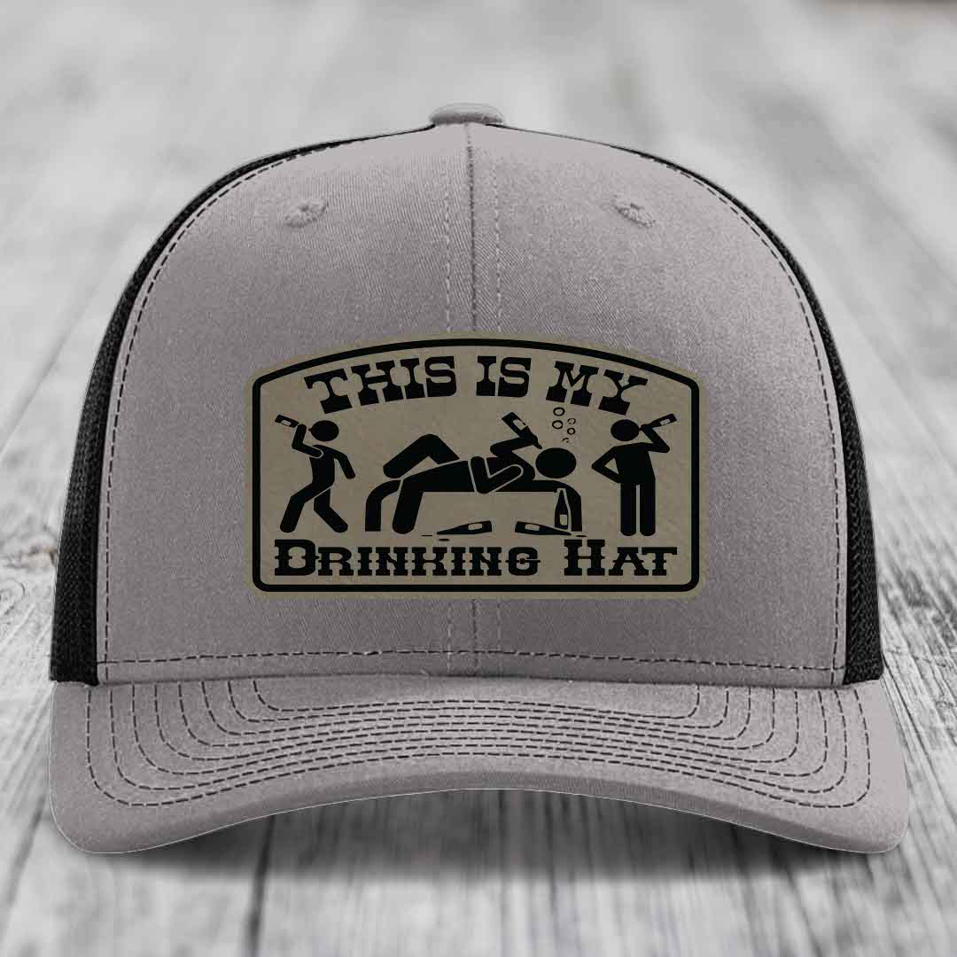 Grey trucker hat with black mesh back and a beige leather patch that reads &