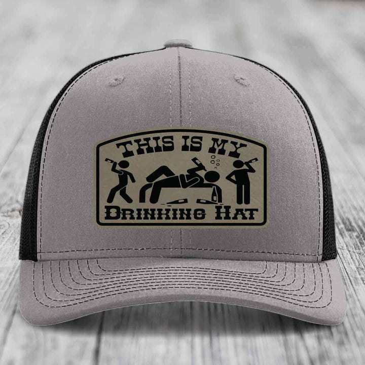 Grey trucker hat with black mesh back and a beige leather patch that reads &