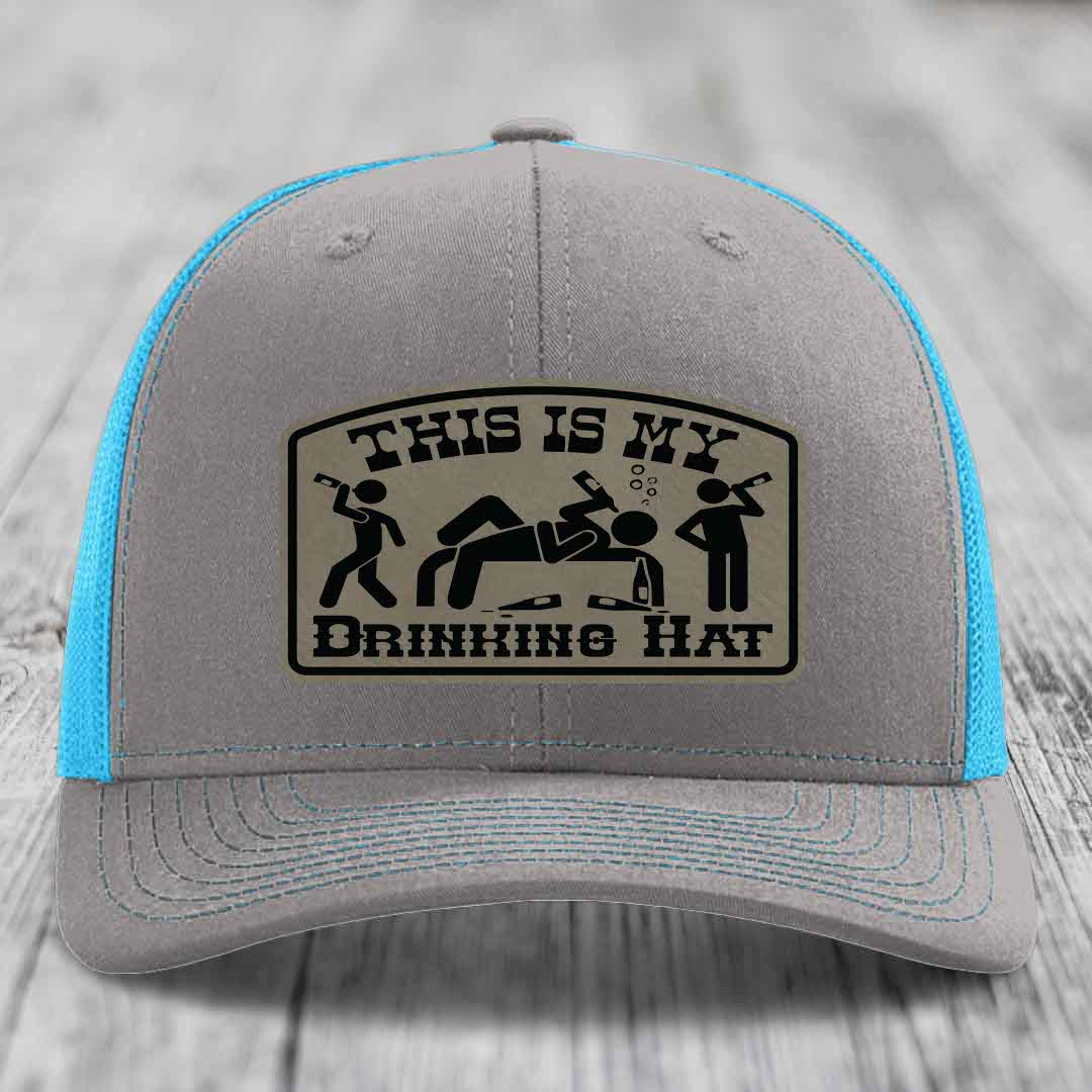 Grey trucker hat with blue mesh back and black leather patch reading &