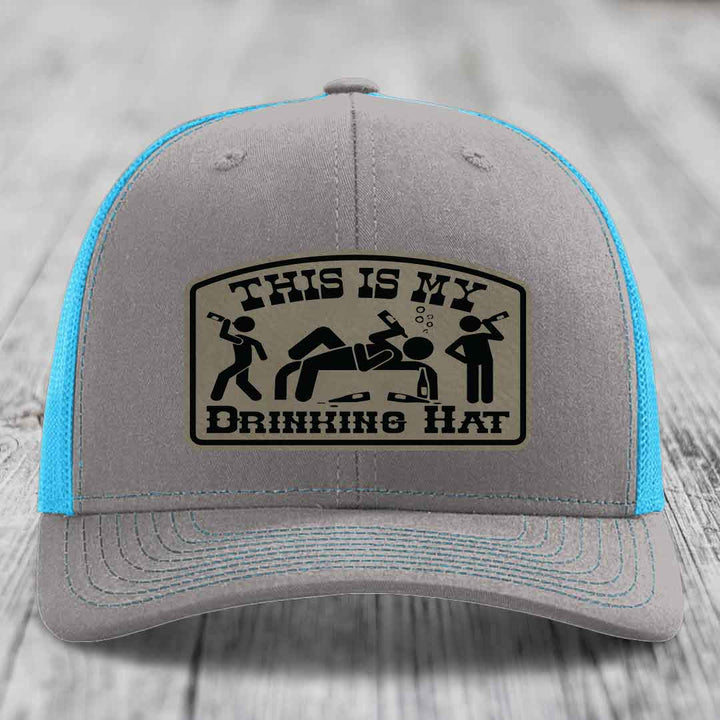 Grey trucker hat with blue mesh back and black leather patch reading &