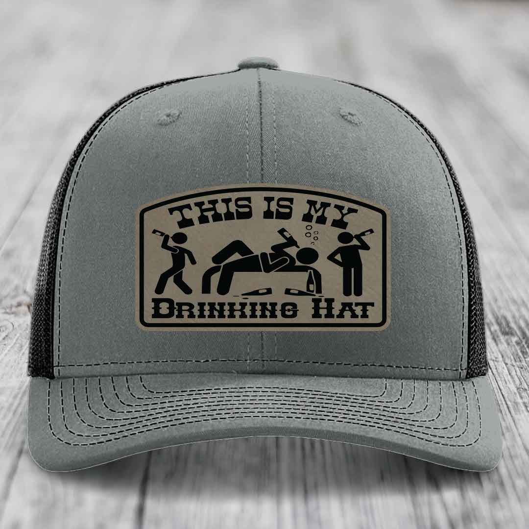 Grey trucker hat with black mesh back and a beige leather patch that reads &