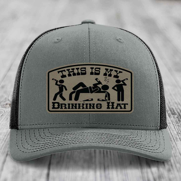 Grey trucker hat with black mesh back and a beige leather patch that reads &