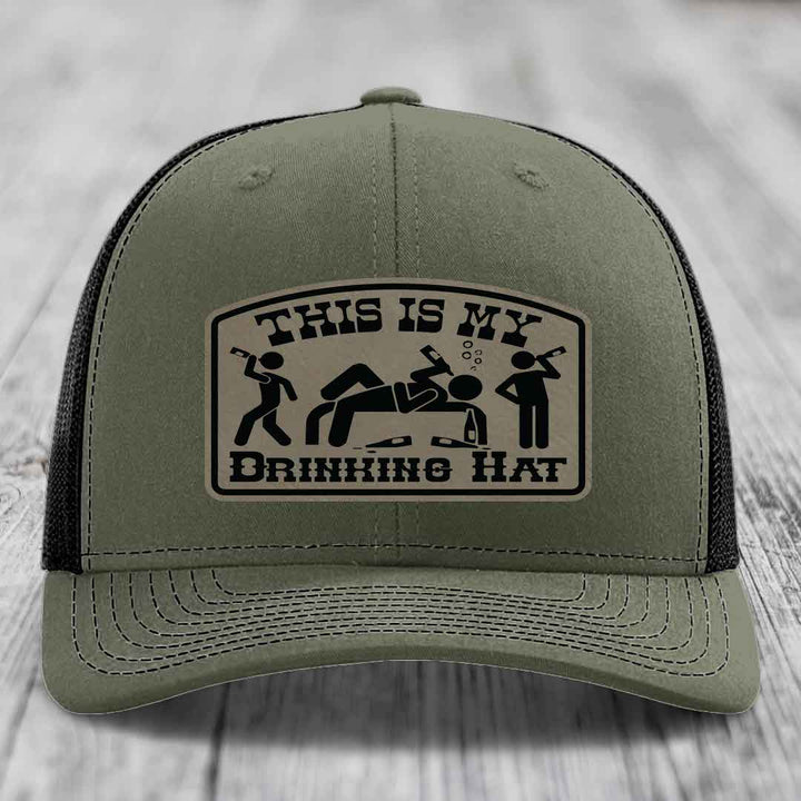 Olive green trucker hat with black mesh back and a beige leather patch reading &