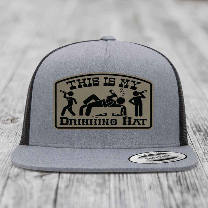 Grey trucker hat with black mesh back and a beige leatherette patch reading &