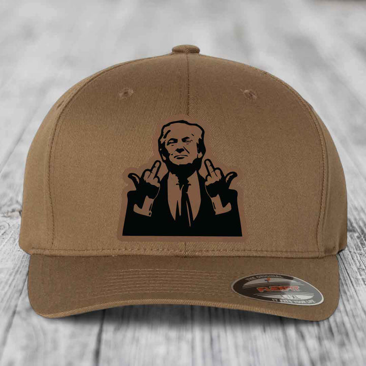 Tan baseball cap with black graphic patch of man making hand gestures, Flexfit brand label visible.