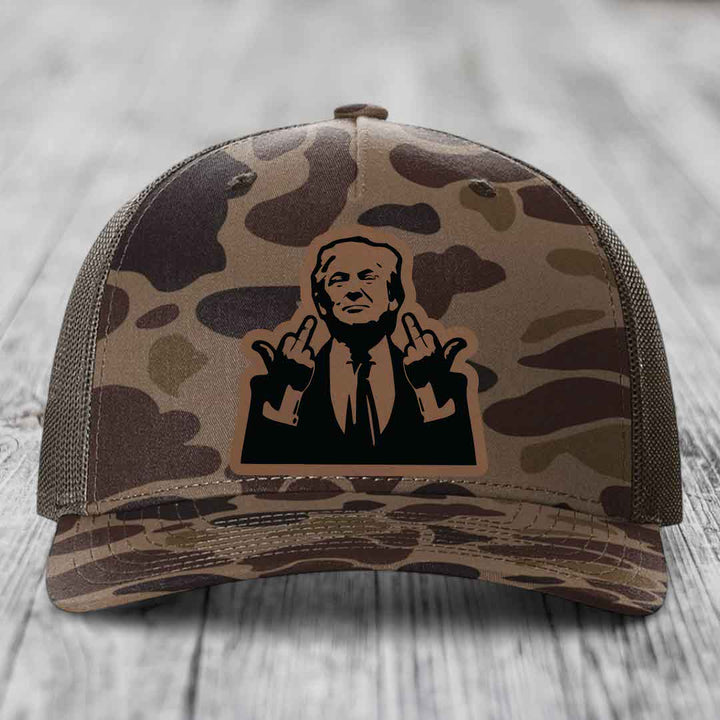 Camouflage trucker hat with black leather patch of man giving middle finger gesture.
