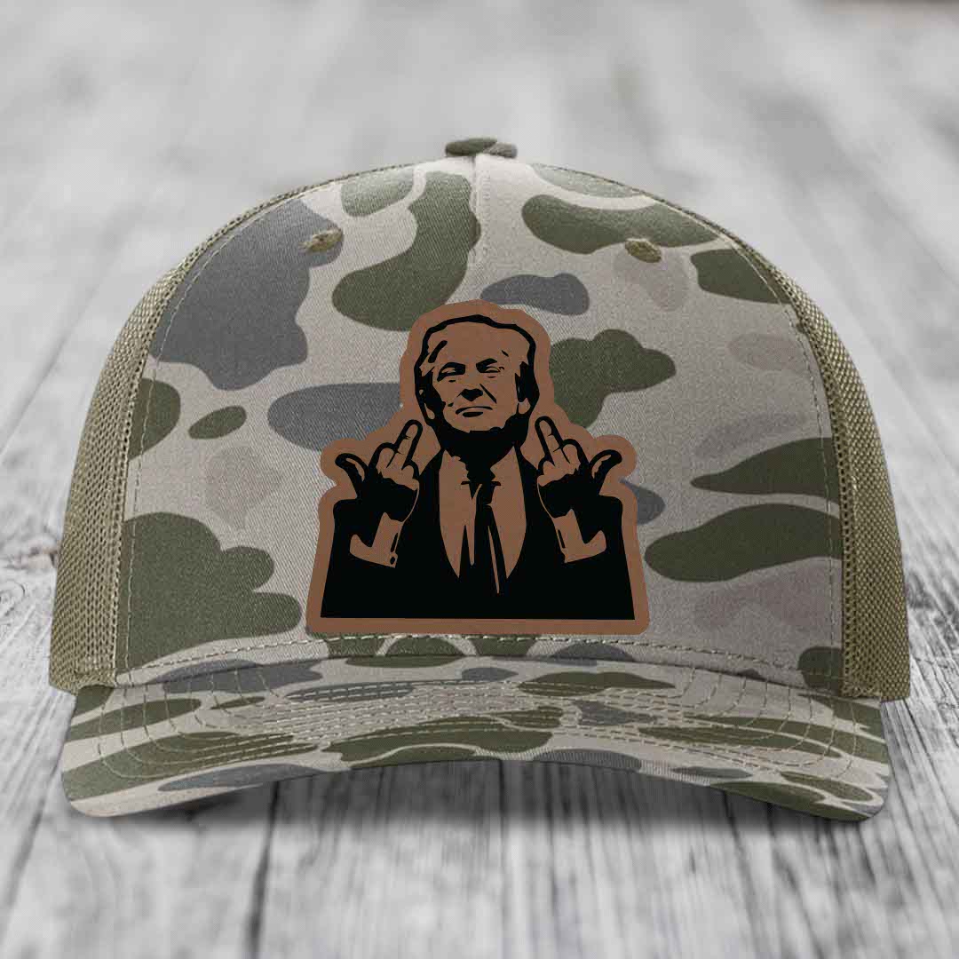 Camouflage trucker hat with a brown and black leatherette patch of a man making hand gestures.