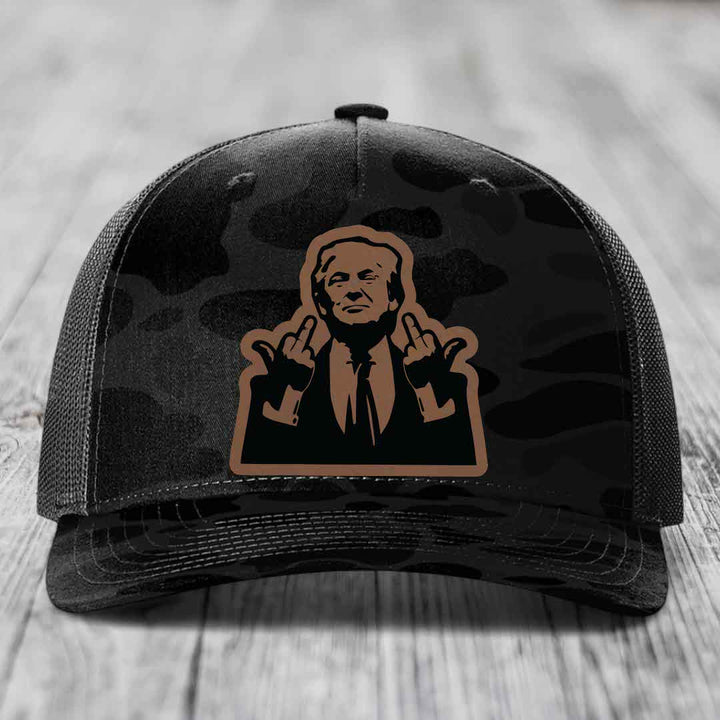 Black camouflage trucker hat with a brown leather patch featuring a cartoon of a man giving two middle fingers.