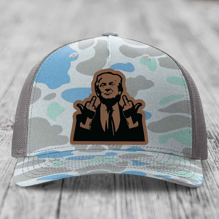 Camouflage trucker hat with a brown leather patch featuring a cartoon of a man making hand gestures.