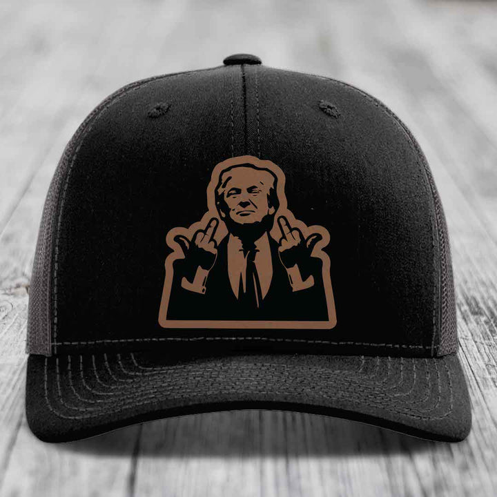 Black trucker hat with brown leather patch of man making rude hand gesture.