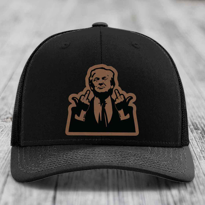 Black trucker hat with brown leather patch of man making rude hand gesture.