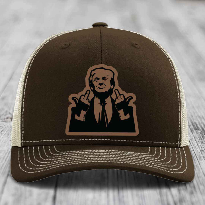 Brown trucker hat with white stitching and a black leatherette patch of a man making hand gestures.