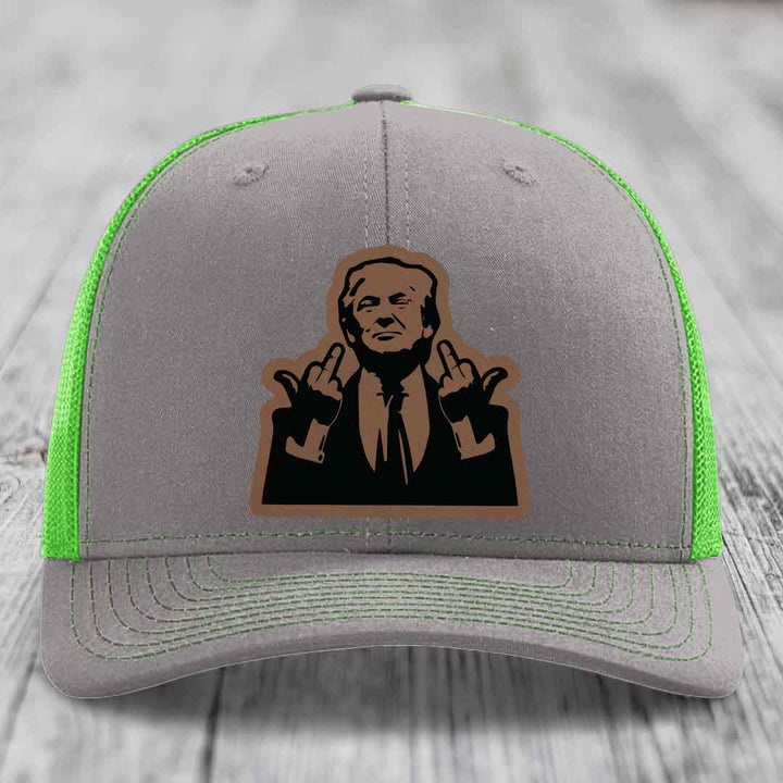 Grey trucker hat with neon green mesh and stitching, featuring a brown leatherette patch of a man making hand gestures.