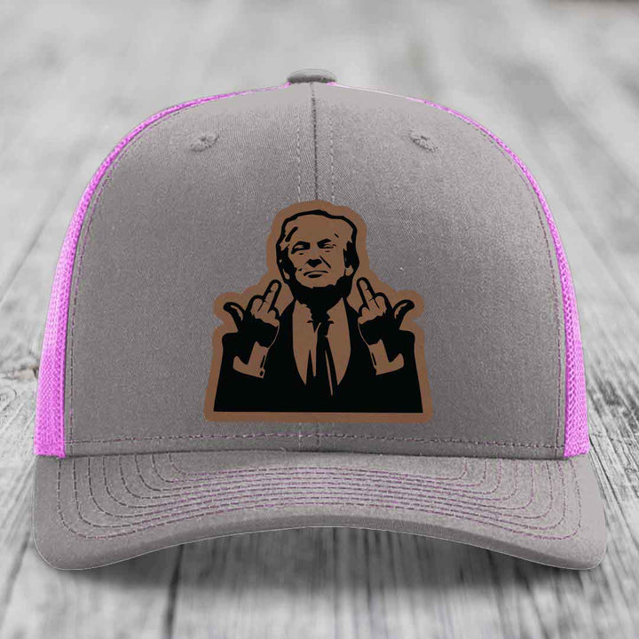 Grey trucker hat with pink mesh sides and a black leatherette patch of a man making rude gestures.