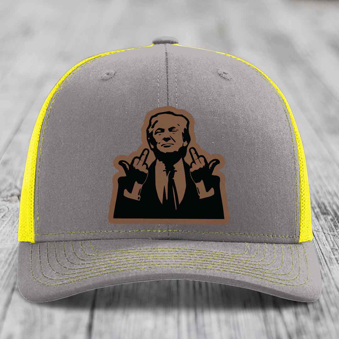 Grey trucker hat with yellow mesh sides and stitching, featuring a brown leatherette patch of a man making hand gestures.