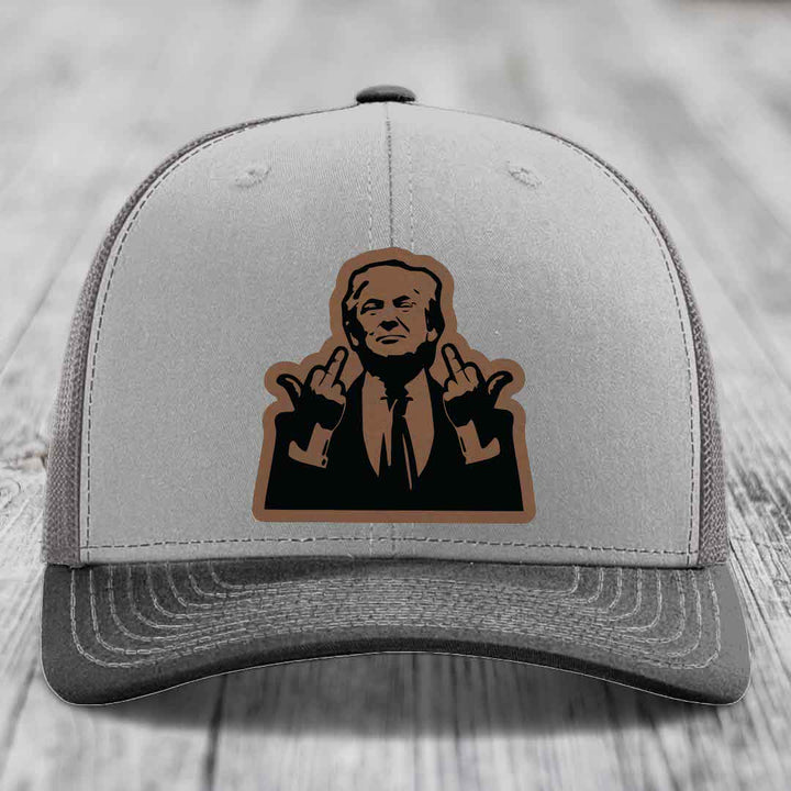 Grey trucker hat with brown and black leather patch of man making rude hand gestures.