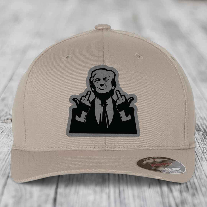 Beige baseball cap with black and grey graphic of man making hand gestures, on wooden surface.