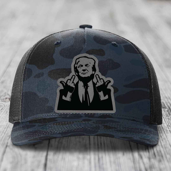 Camouflage trucker hat with black and grey patch of man making rude hand gestures.
