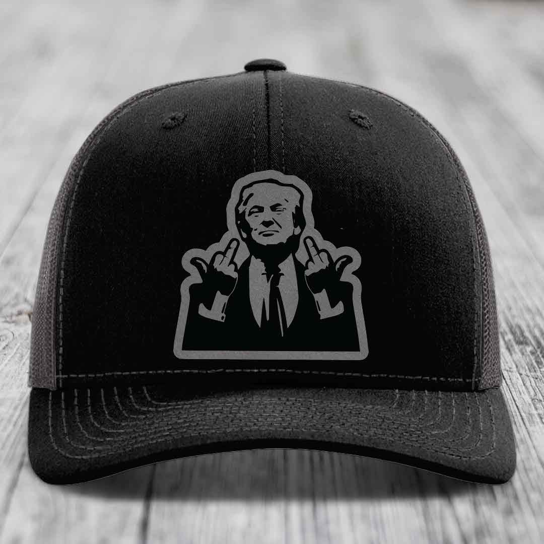 Black trucker hat with gray graphic of man making hand gestures, on wooden surface.