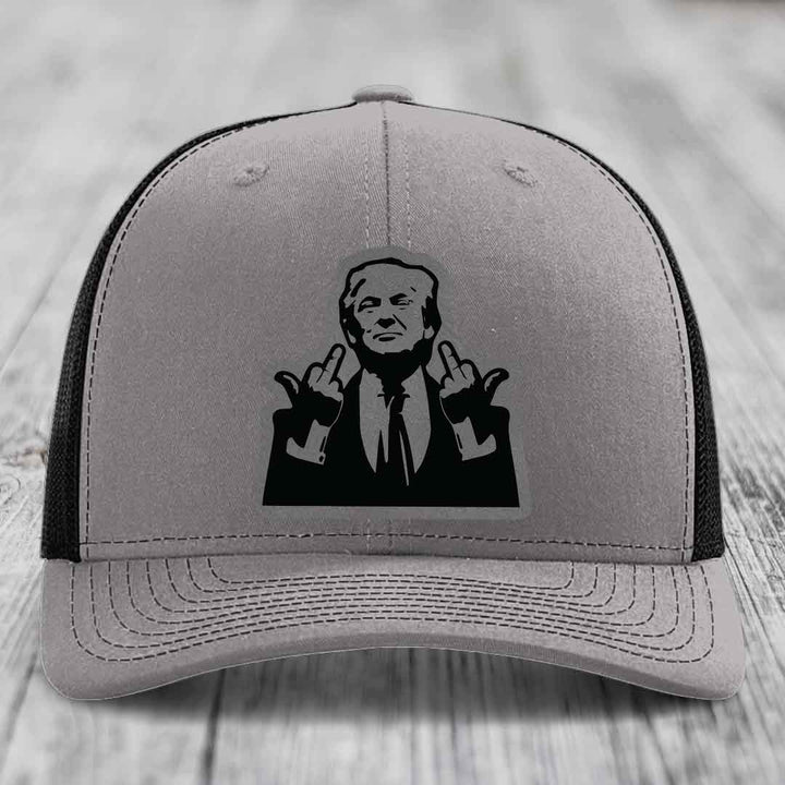 Grey trucker hat with black mesh back and a black leatherette patch of a man making a rude gesture.