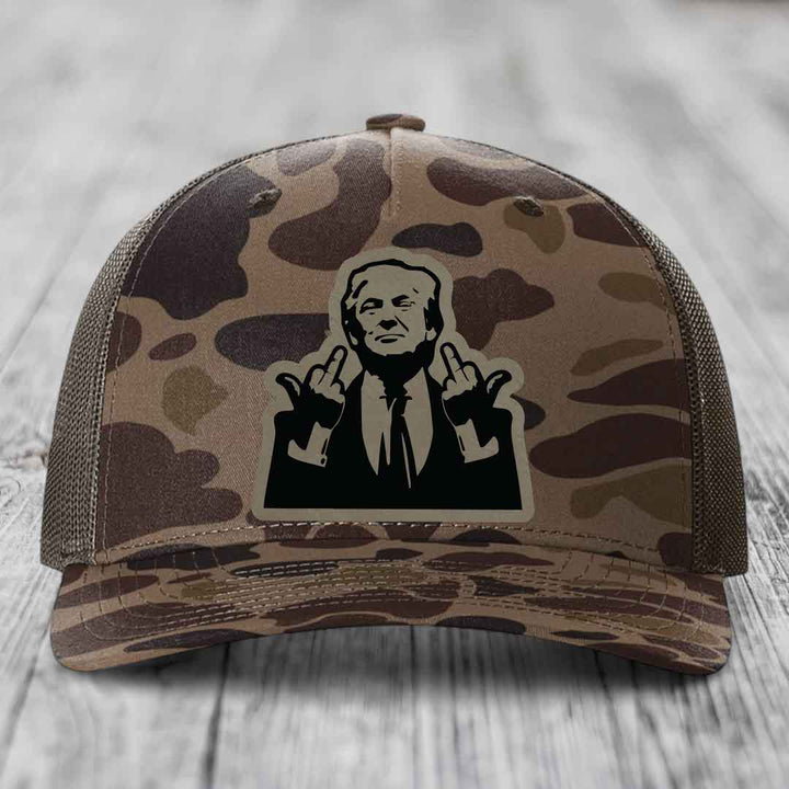 Camouflage trucker hat with a black and beige patch of a man making rude hand gestures.