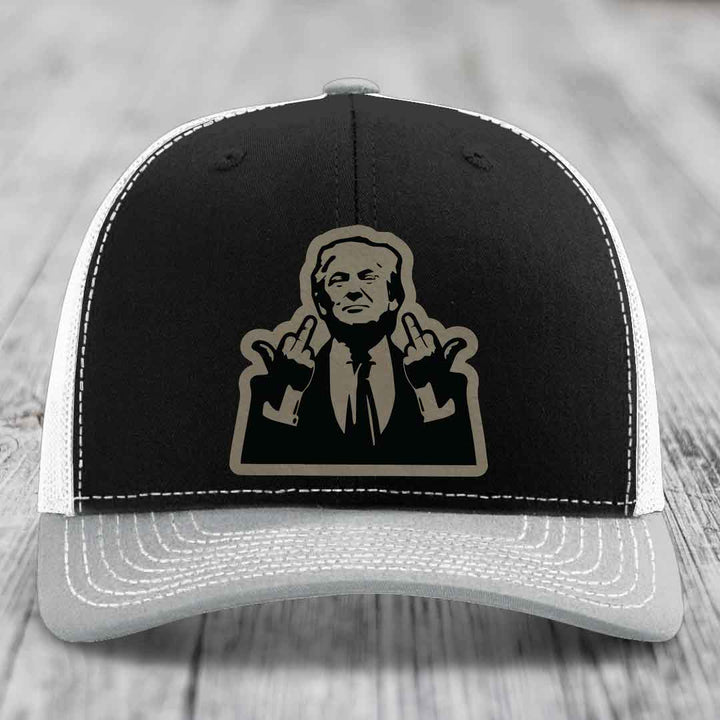 Black and grey trucker hat with white stitching and a beige graphic patch of a man making rude hand gestures.