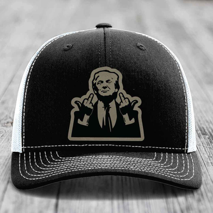 Black trucker hat with white stitching and a beige patch of a man making rude hand gestures.