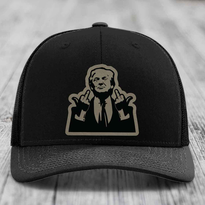 Black trucker hat with beige silhouette patch of a man making rude hand gestures.