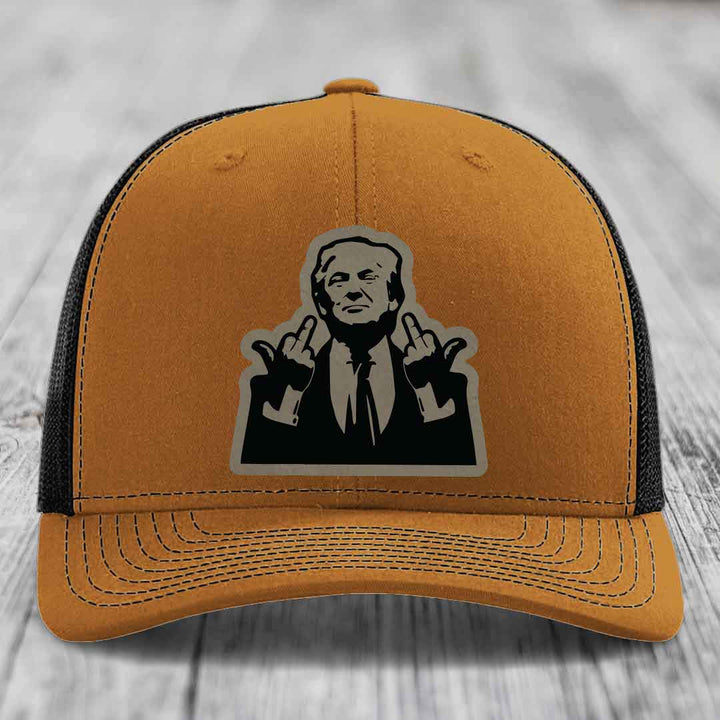 Tan trucker hat with black mesh back and a black-and-grey graphic patch of a man making hand gestures.