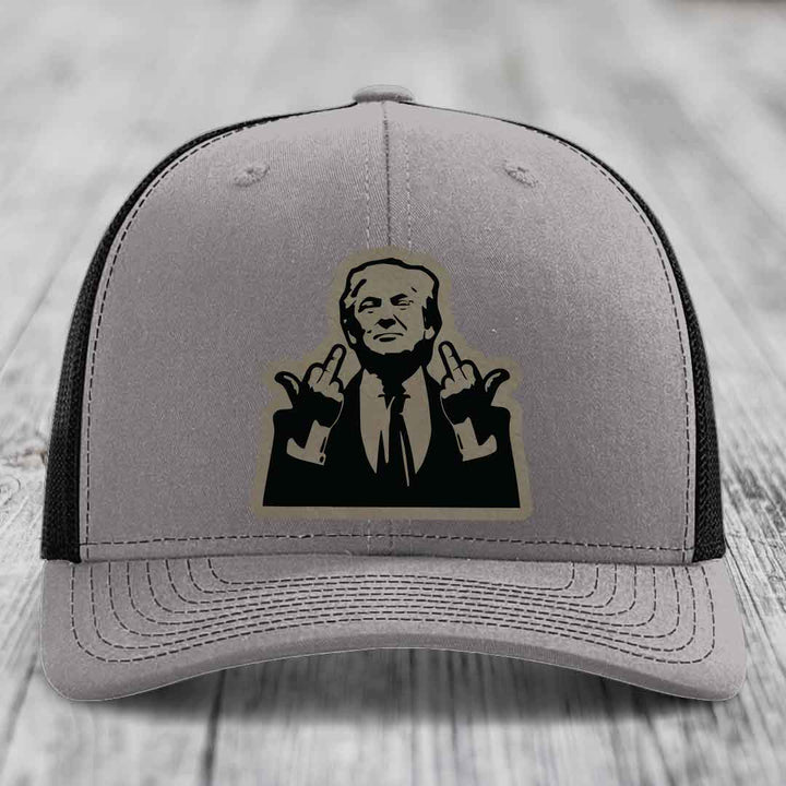 Grey trucker hat with black mesh back and a black leatherette patch of a man giving two middle fingers.