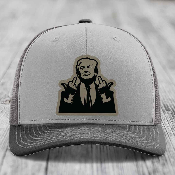 Grey trucker hat with black and tan patch of man giving middle finger gesture.