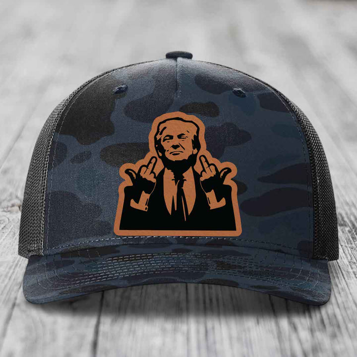 Camouflage trucker hat with a brown leather patch featuring a silhouette of a man making hand gestures.