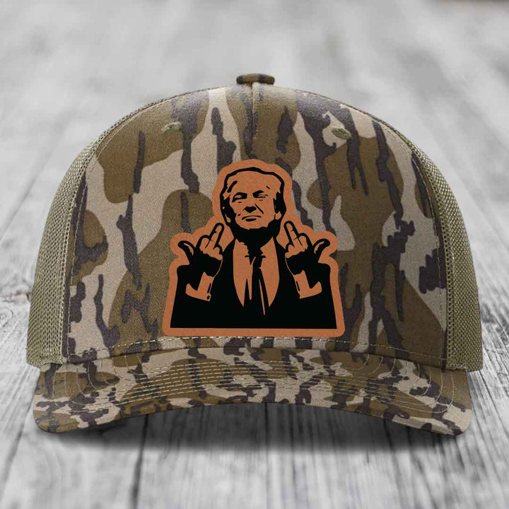 Camouflage trucker hat with orange and black leather patch of a man giving middle fingers.