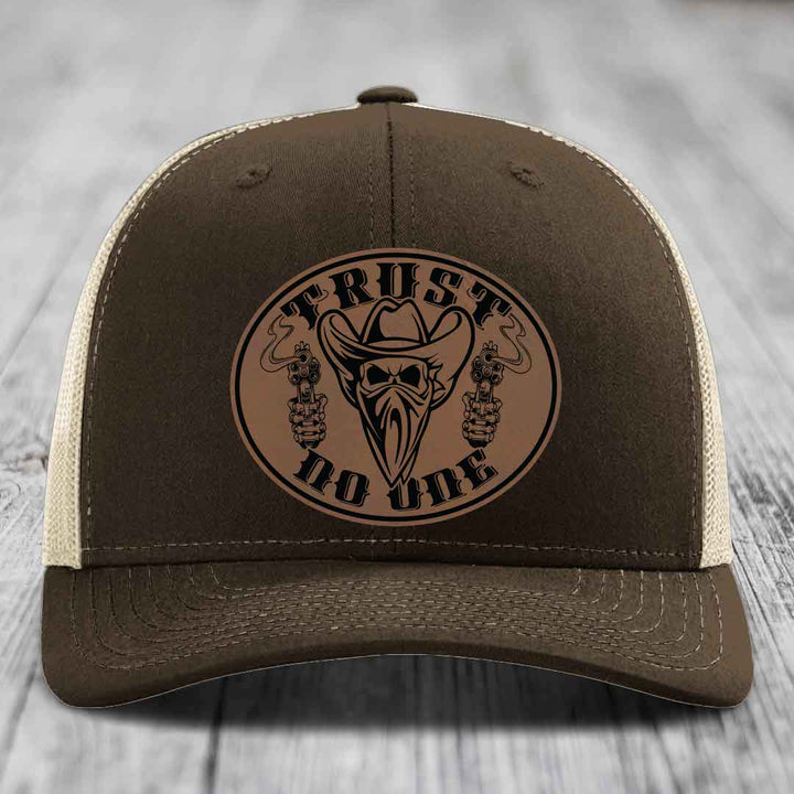 Brown trucker hat with a circular leather patch featuring a masked cowboy holding two pistols and the text &
