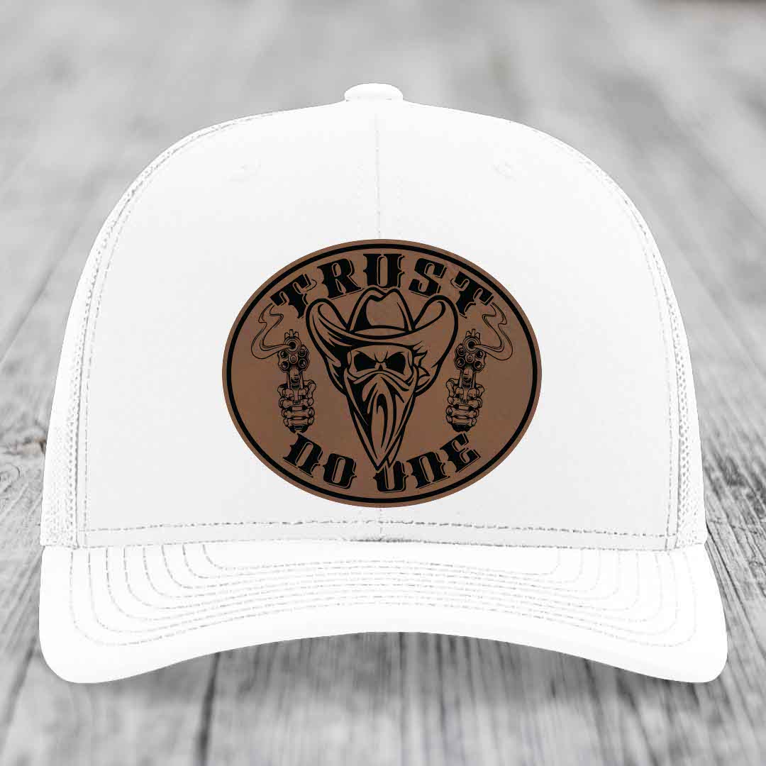 White trucker hat with brown leather patch featuring skull, cowboy hat, and guns with &
