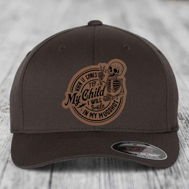 Dark brown Flexfit hat with a tan leatherette patch featuring a skeleton holding up peace signs and text reading &