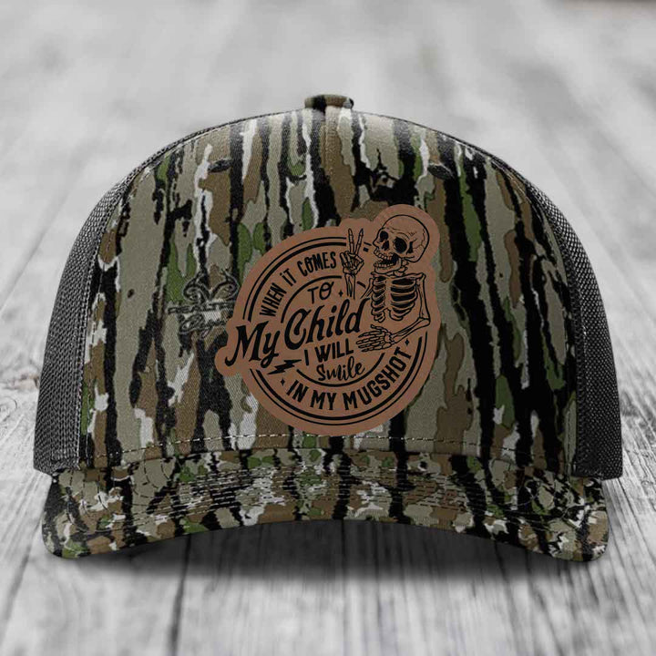 Camouflage trucker hat with brown leather patch featuring skeleton and text &