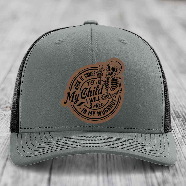 Grey trucker hat with brown leather patch featuring skeleton and text &