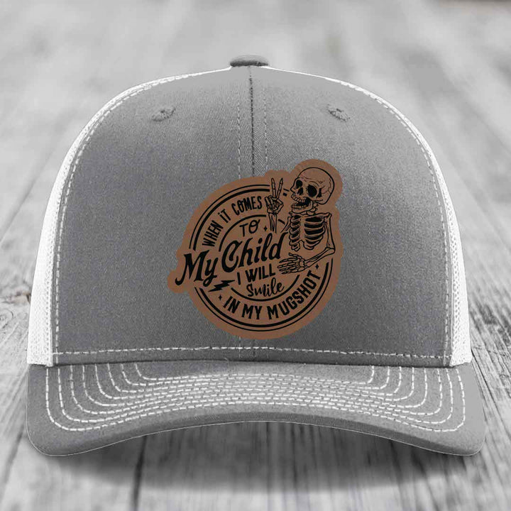 Grey trucker hat with brown leather patch featuring skeleton and text &