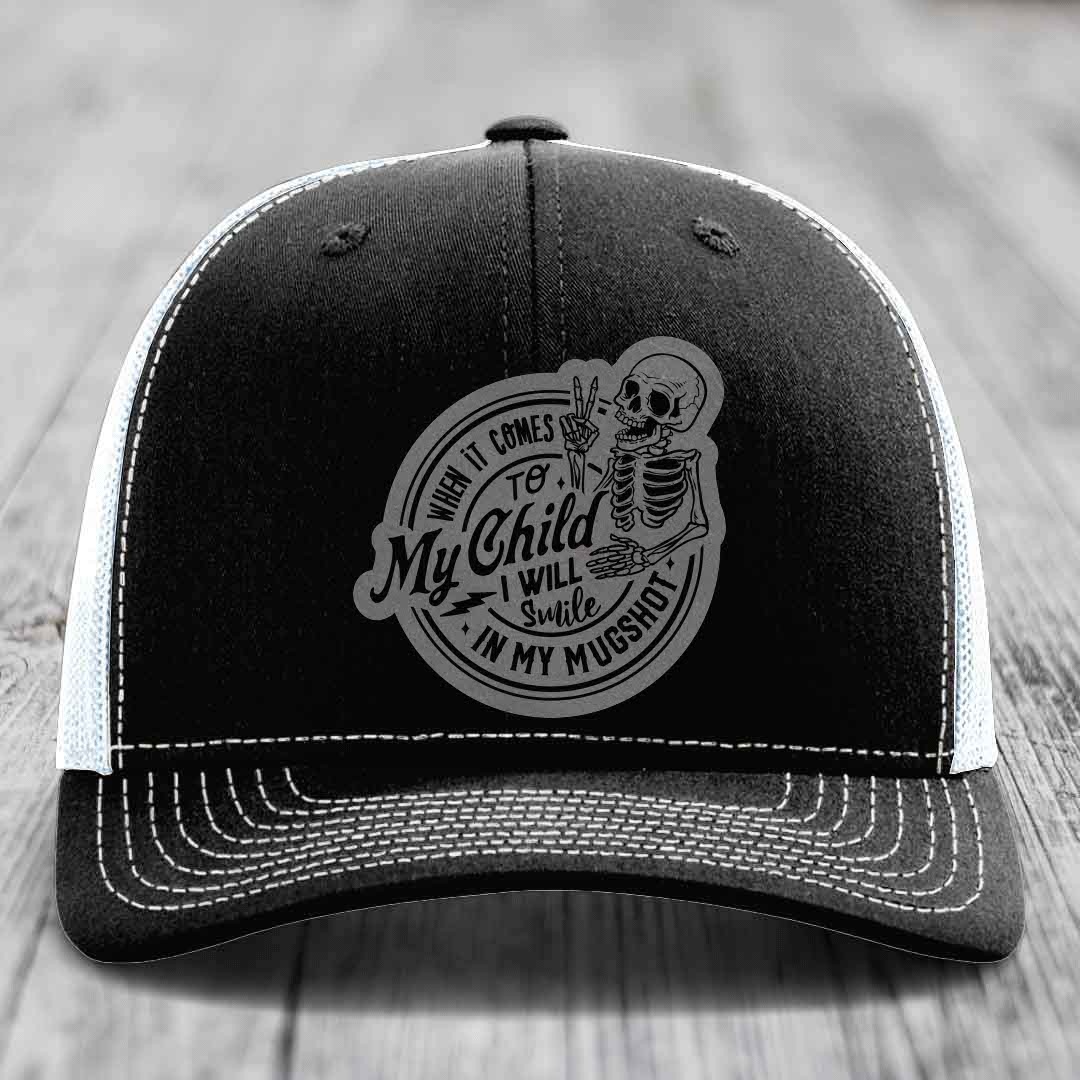 Black trucker hat with white stitching and a gray skull patch reading &