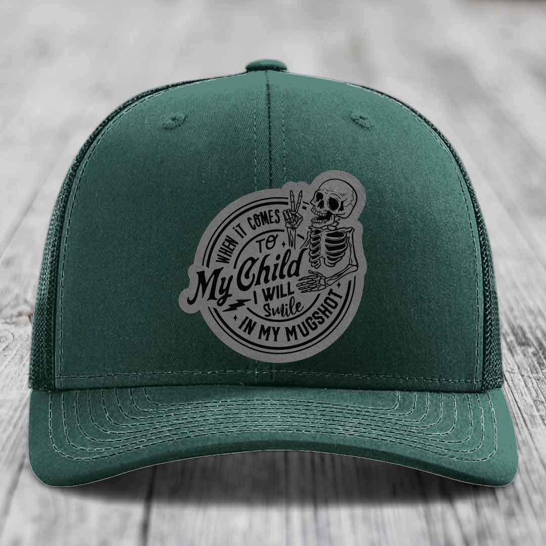 Dark green trucker hat with a grey circular patch featuring a skeleton holding a peace sign and text: &