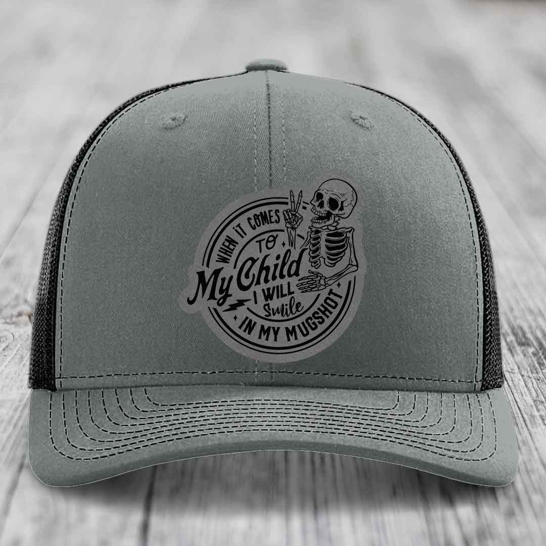 Grey trucker hat with black mesh back and a circular patch featuring a skeleton holding up two fingers and the text &