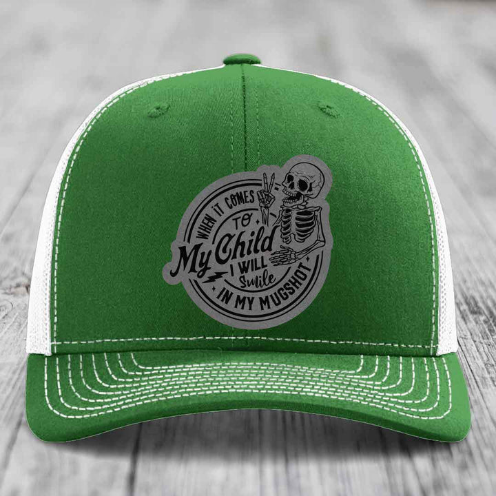 Green trucker hat with white mesh back and gray skull patch reading &