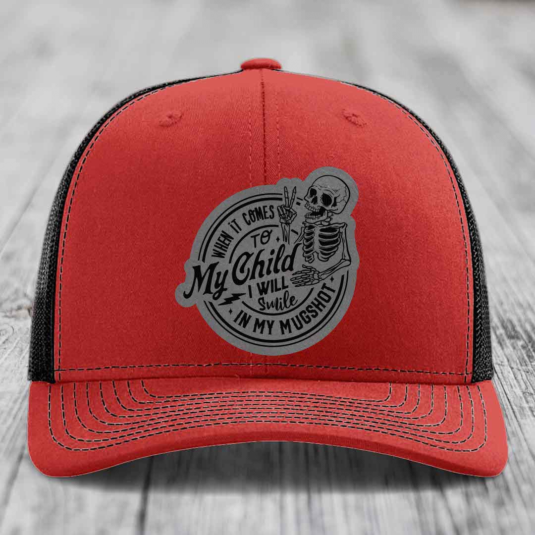 Red trucker hat with grey circular patch showing skeleton making peace sign and text &