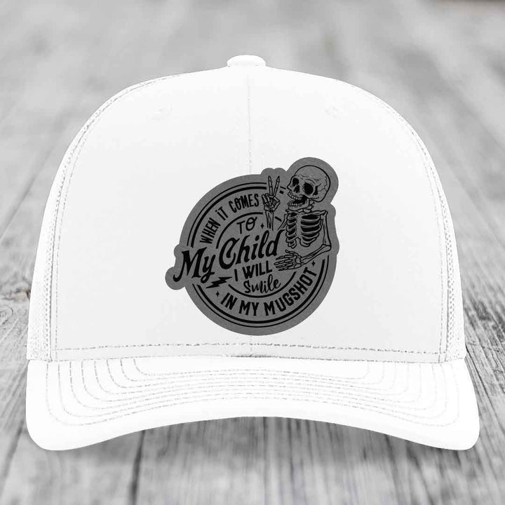 White trucker hat with black circular patch featuring skeleton and text &