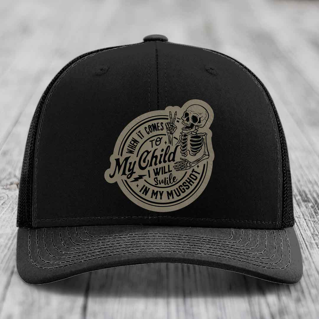 Black trucker hat with a beige circular patch featuring a skeleton and the text &