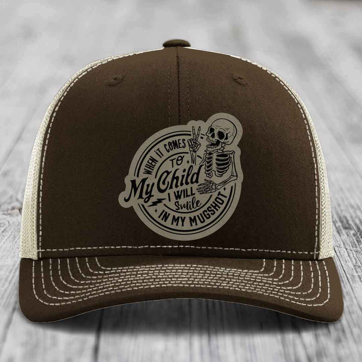Brown trucker hat with white stitching and a skull patch reading &